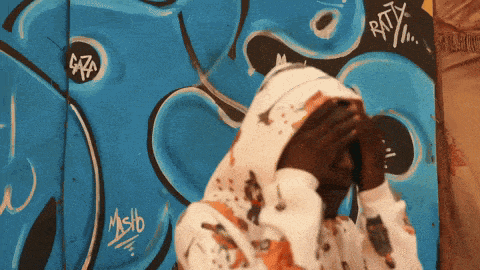 a person wearing a white hoodie covering their face in front of a graffiti wall