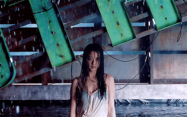 a woman in a white dress is standing in the rain in front of a green sign