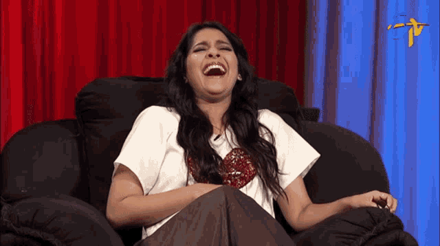 a woman is sitting in a chair and laughing with a tv logo in the background