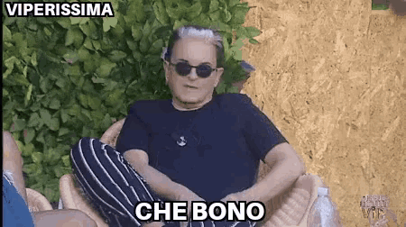 a man wearing sunglasses and a black shirt is sitting in a chair with the words che bono above him