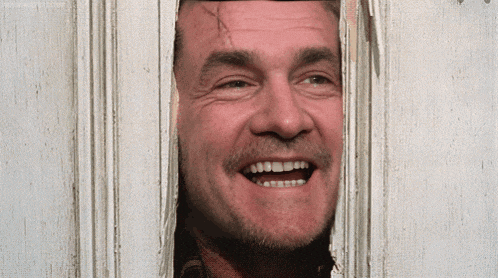a man with a beard is smiling while looking through a hole in a door