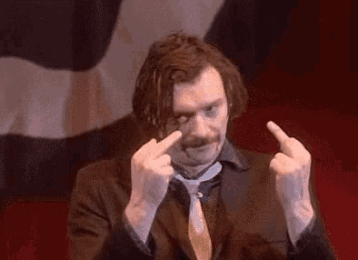 a man in a suit and tie is making a middle finger sign .