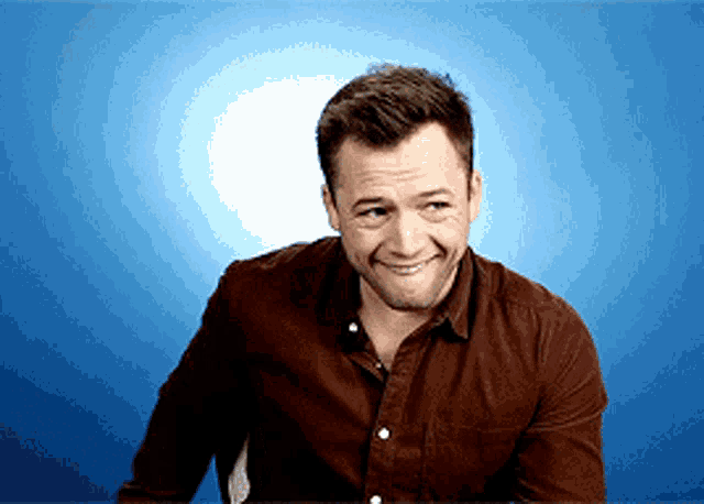a man in a brown shirt is smiling in front of a blue wall