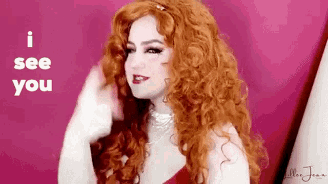 a woman with red curly hair is standing in front of a pink background .