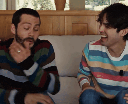 two men wearing striped sweaters are sitting on a couch laughing