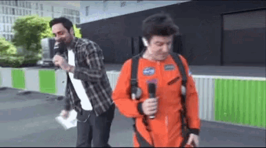 a man in an orange space suit is holding a microphone while another man talks into it