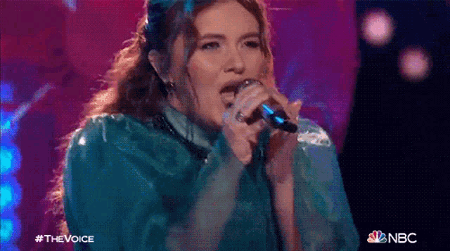 a woman in a blue dress is singing into a microphone on stage .