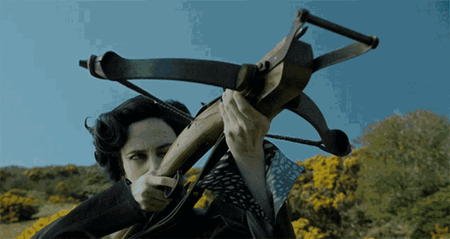 a woman holding a crossbow with a blue sky behind her