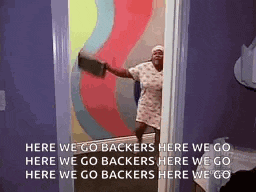 a woman is standing in a doorway holding a broom and a sign that says `` here we go backers here we go ''