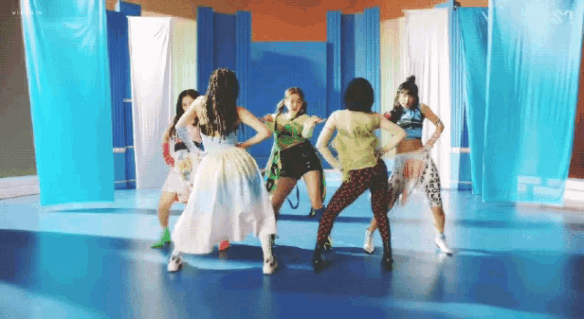 a group of young women are dancing in a room with blue curtains