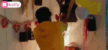 a man in a yellow shirt is holding a heart shaped balloon in a room .