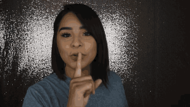 a woman holds her finger to her lips in a gesture of silence