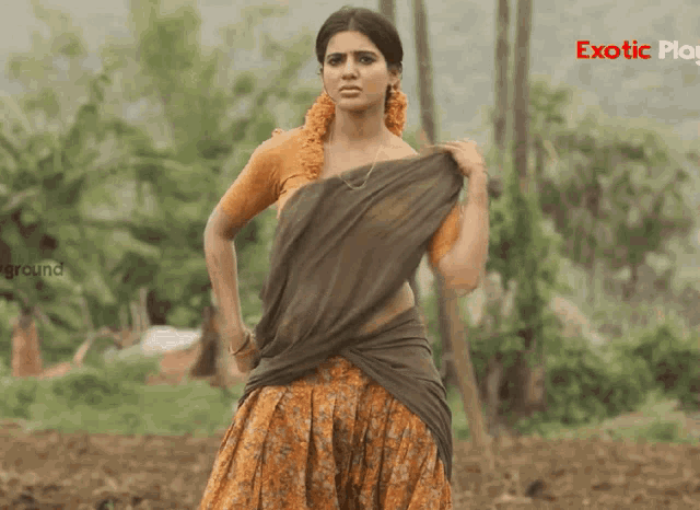 a woman in a saree is standing in a field with the word exotic on the bottom right