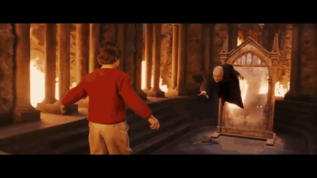 a boy in a red sweater stands in front of a mirror with a man in a black robe behind it