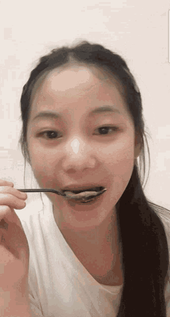 a woman in a white shirt holds a spoon in her mouth