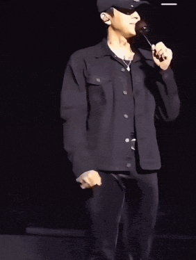 a man wearing a black hat and sunglasses is holding a microphone