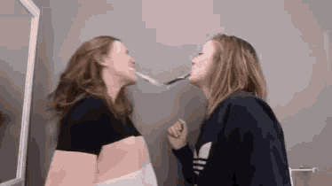 two women brushing their teeth in front of a mirror and one has an adidas sweatshirt on