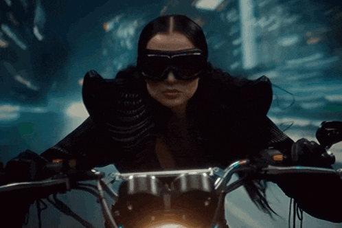 a woman wearing sunglasses and a black jacket rides a motorcycle