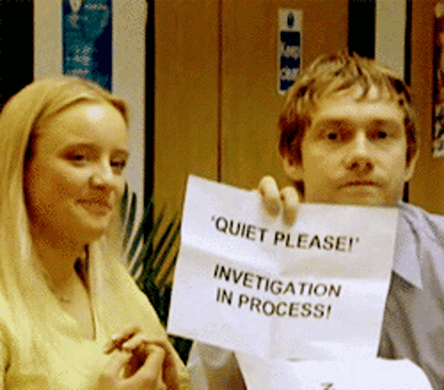 a man and a woman are holding a piece of paper that says quiet please