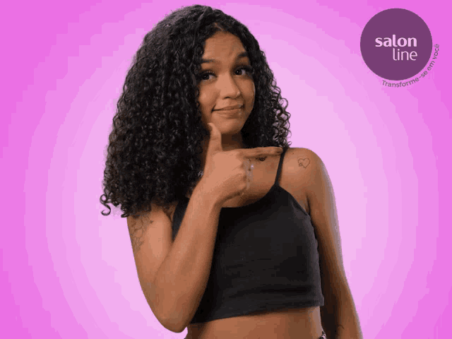 a woman with curly hair is pointing at her tattoo on her shoulder in front of a salon line logo