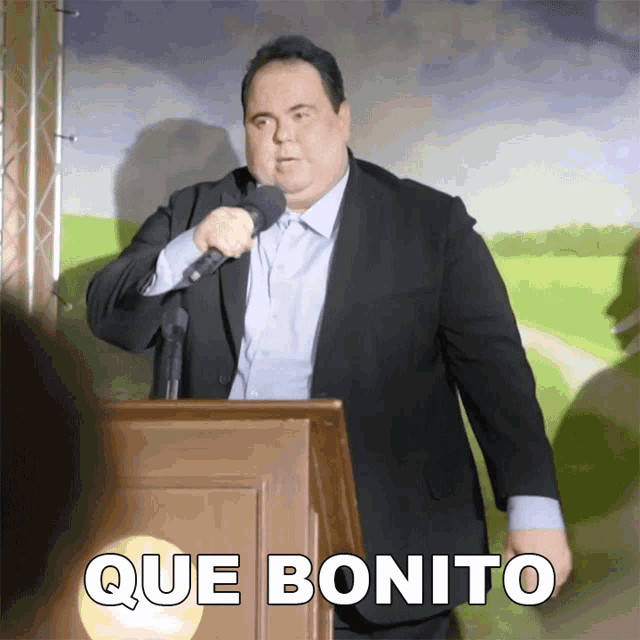 a man in a suit stands at a podium with que bonito written on the bottom
