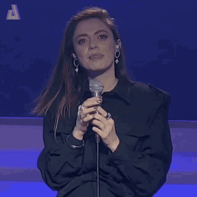 a woman is smiling while holding a microphone and wearing a black jacket .