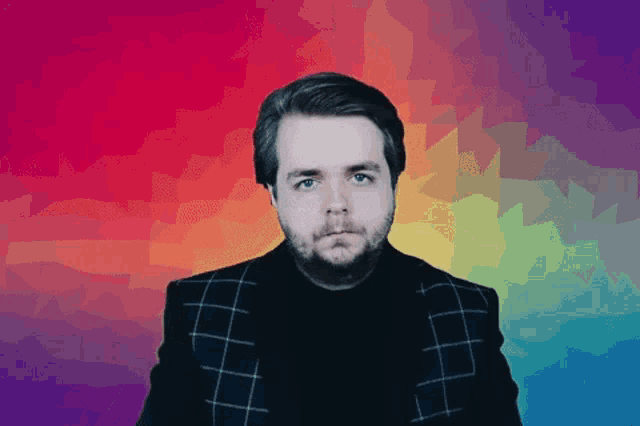 a man with a beard is standing in front of a rainbow backdrop