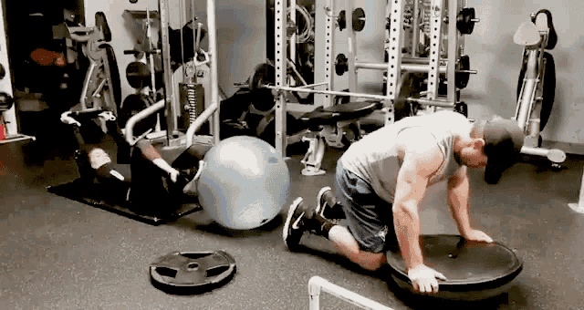 a man is kneeling on a platform in a gym while a woman sits on a ball