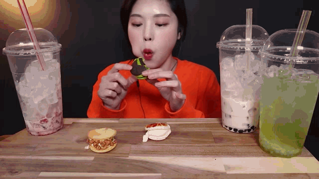 a woman sits at a table eating a sandwich and drinking iced beverages