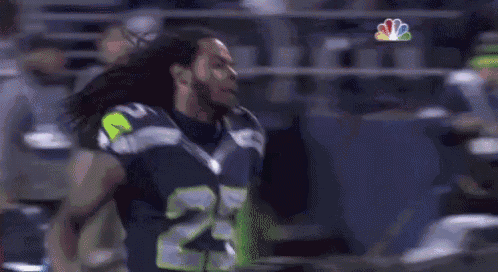 a man in a seahawks jersey is standing on a field .