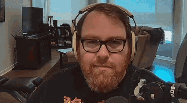 a man with glasses and a beard wears headphones and a rode microphone