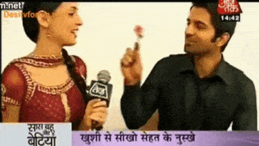 a man is holding a flower and talking to a woman on a television screen