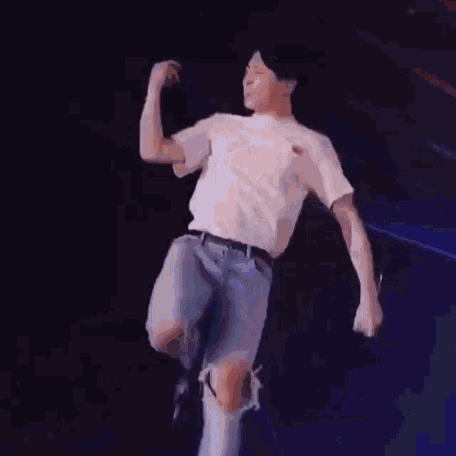 a man in a white shirt and blue jeans is dancing on stage .
