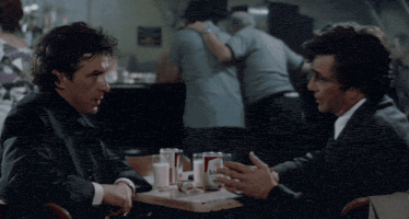two men are sitting at a table with a soda can that says sol