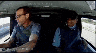 a man in a blue shirt is driving a car with a time stamp of 10:25:10