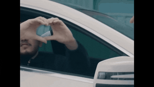 a man is making a heart shape with his hands in a car window