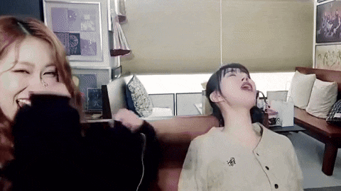 two women are sitting on a couch in a living room laughing .
