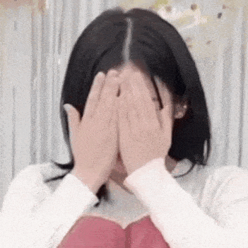 a woman is covering her face with her hands while wearing a white sweater .