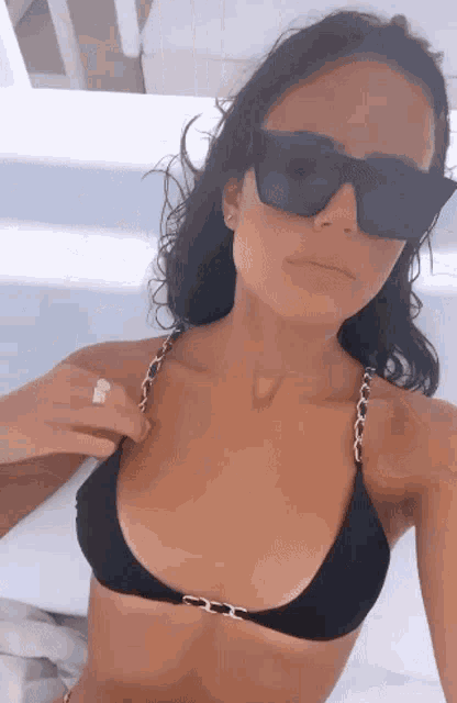a woman in a black bikini and sunglasses is laying on a bed