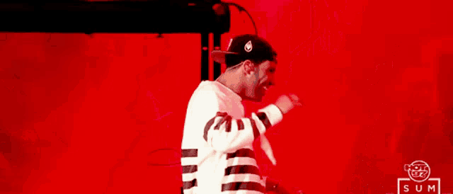 a man wearing a black and white striped shirt is standing in front of a red background with sum written on it