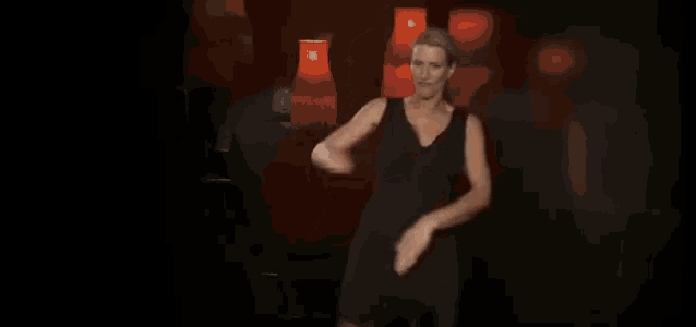 a woman in a black dress is dancing in a dark room with red lamps behind her