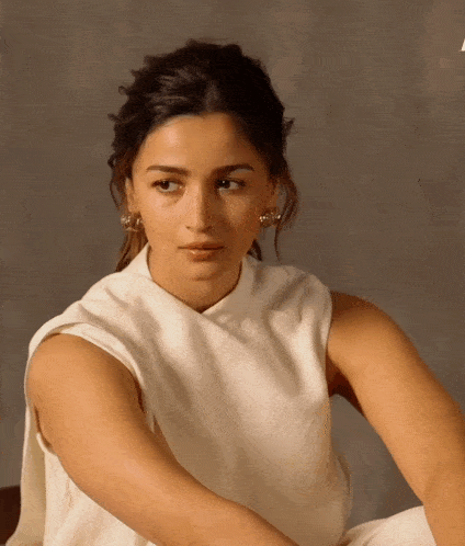 a woman wearing a white top and earrings looks to the side