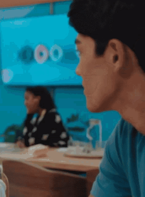 a man in a blue shirt sits at a table with a woman behind him