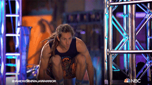 a man with dreadlocks is squatting in front of a nbc sign