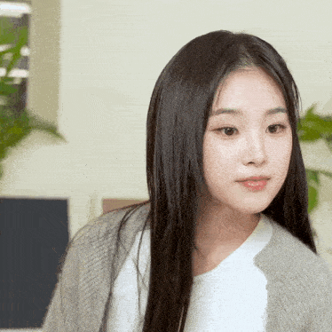 a woman with long black hair wearing a grey cardigan and a white shirt