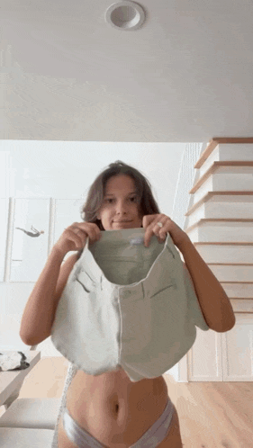 a woman in underwear is holding a pair of shorts over her head .