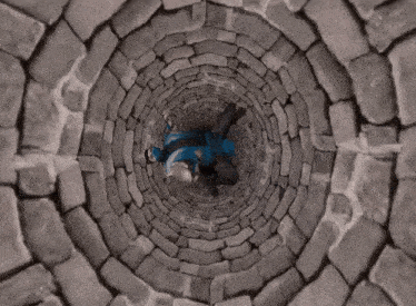 a person in a blue jacket is laying down in a stone well