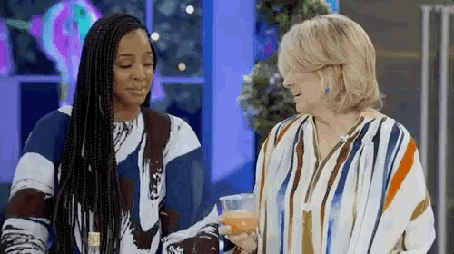 two women are standing next to each other holding glasses of wine .