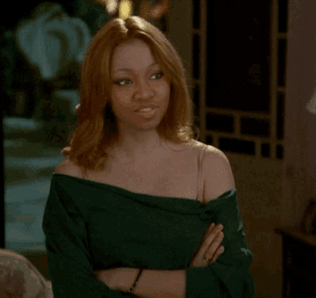 a woman wearing a green off the shoulder top stands with her arms crossed
