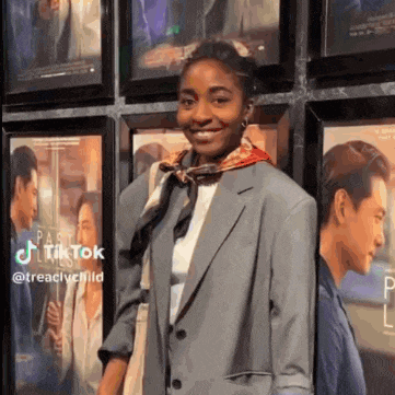 a woman wearing a suit and scarf is standing in front of a wall of movie posters .
